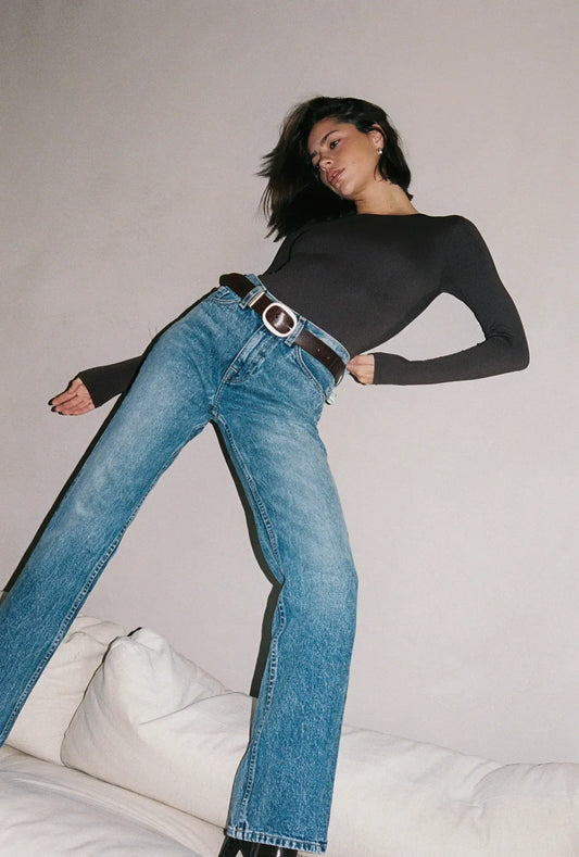 Woman wearing blue jeans and a black top on a plain background