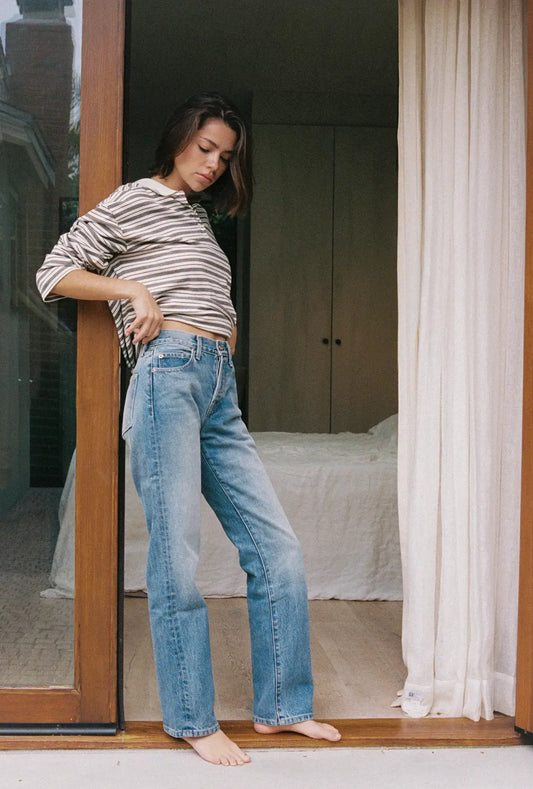 Woman wearing a striped shirt and blue jeans standing in a doorway.