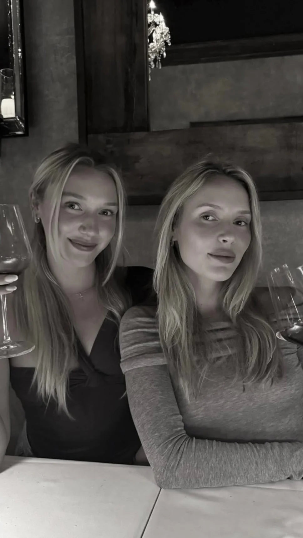 Two women LKBLUE sisters are sitting together in a dimly lit room with a mirror in the background.