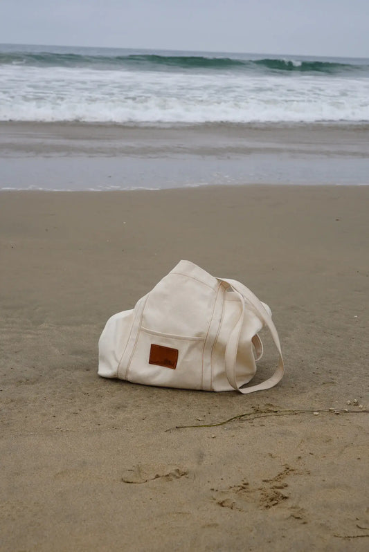 Beige bag on a sandy beach with ocean waves in the background
