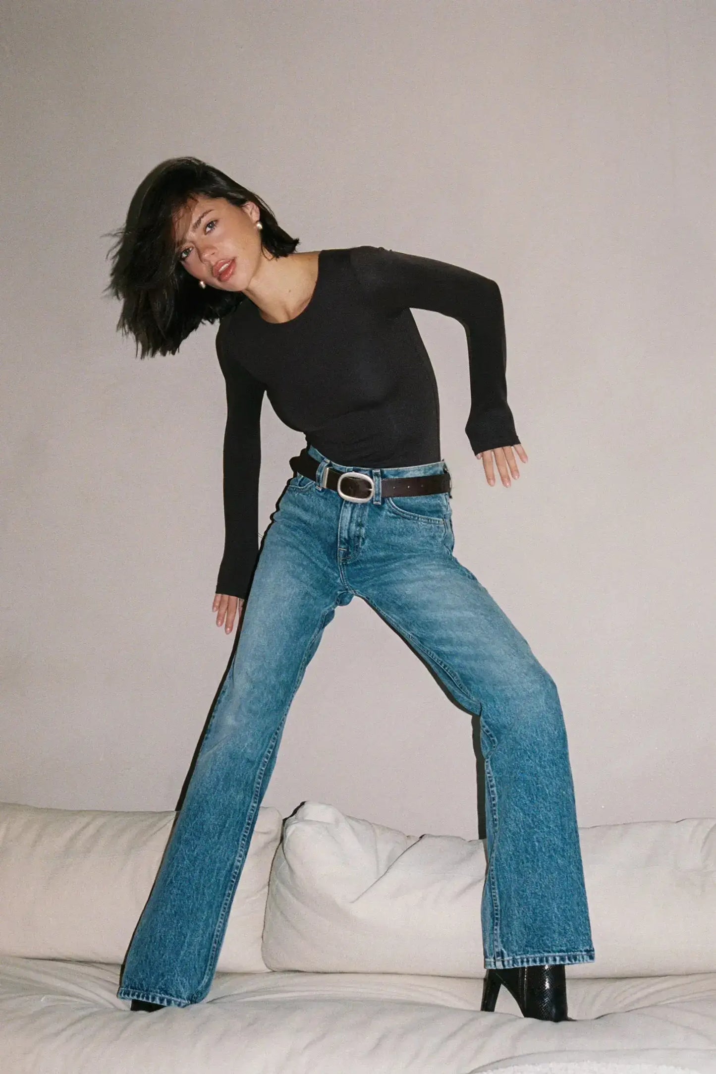 Woman wearing a black top and blue jeans standing on a white surface with a neutral background