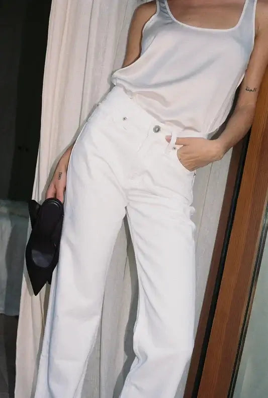 Person wearing a light gray tank top and white bootcut pants with a blurred background