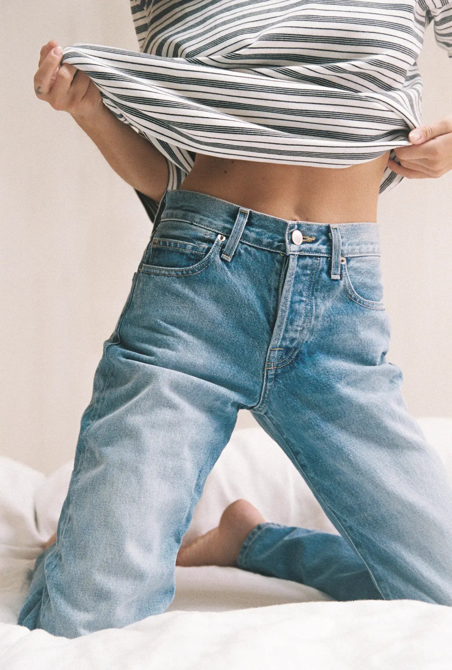 Person wearing a striped crop top and blue jeans on a neutral background