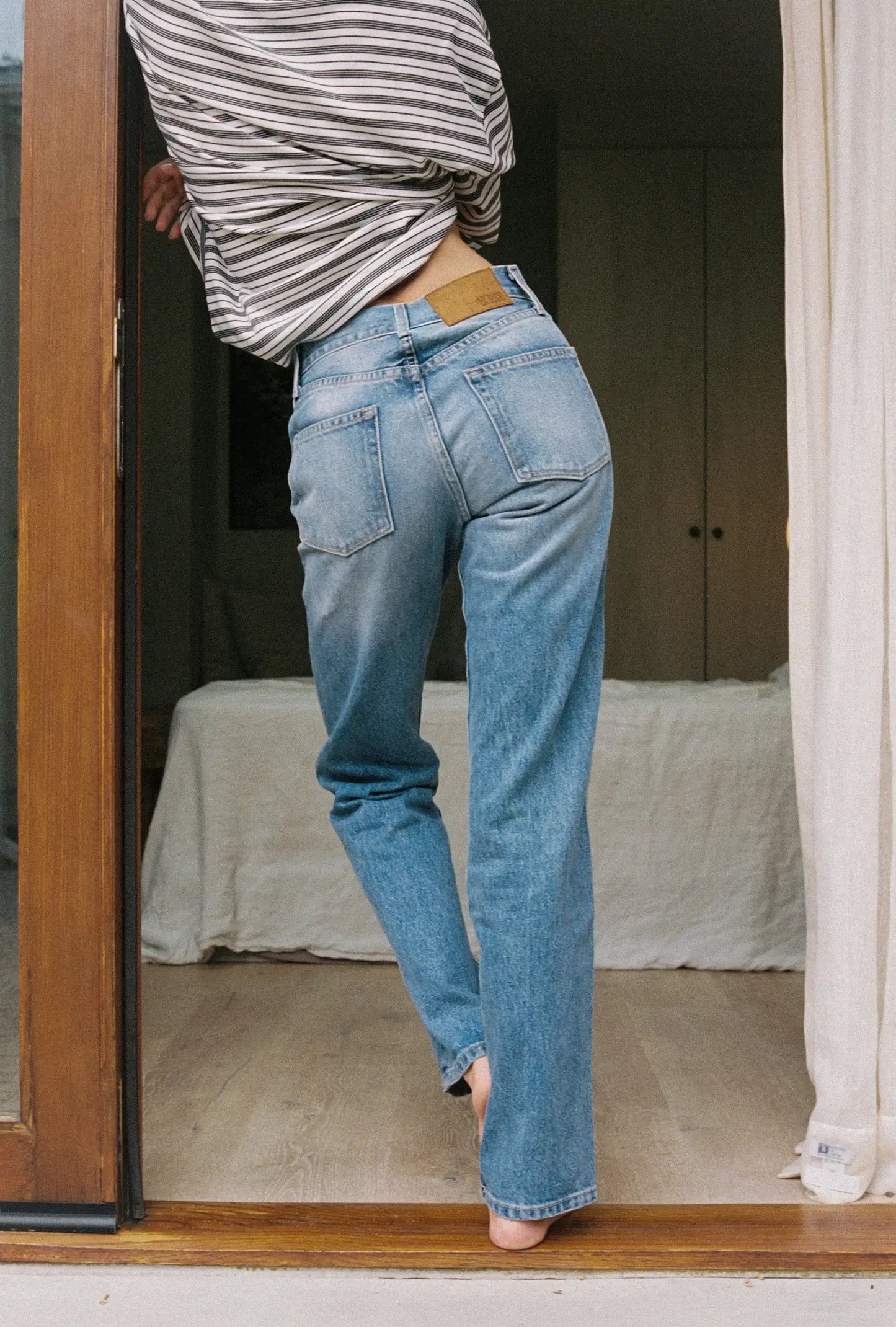 Person wearing blue jeans and a striped shirt standing in a doorway.