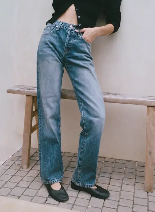 A person wearing high-waisted blue straight leg jeans is sitting on a bench.
