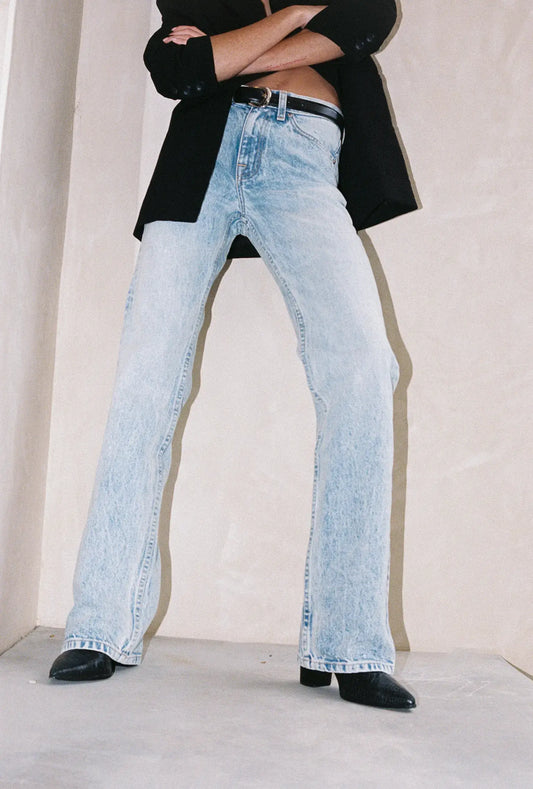 Person wearing light blue jeans and a black jacket with a plain background