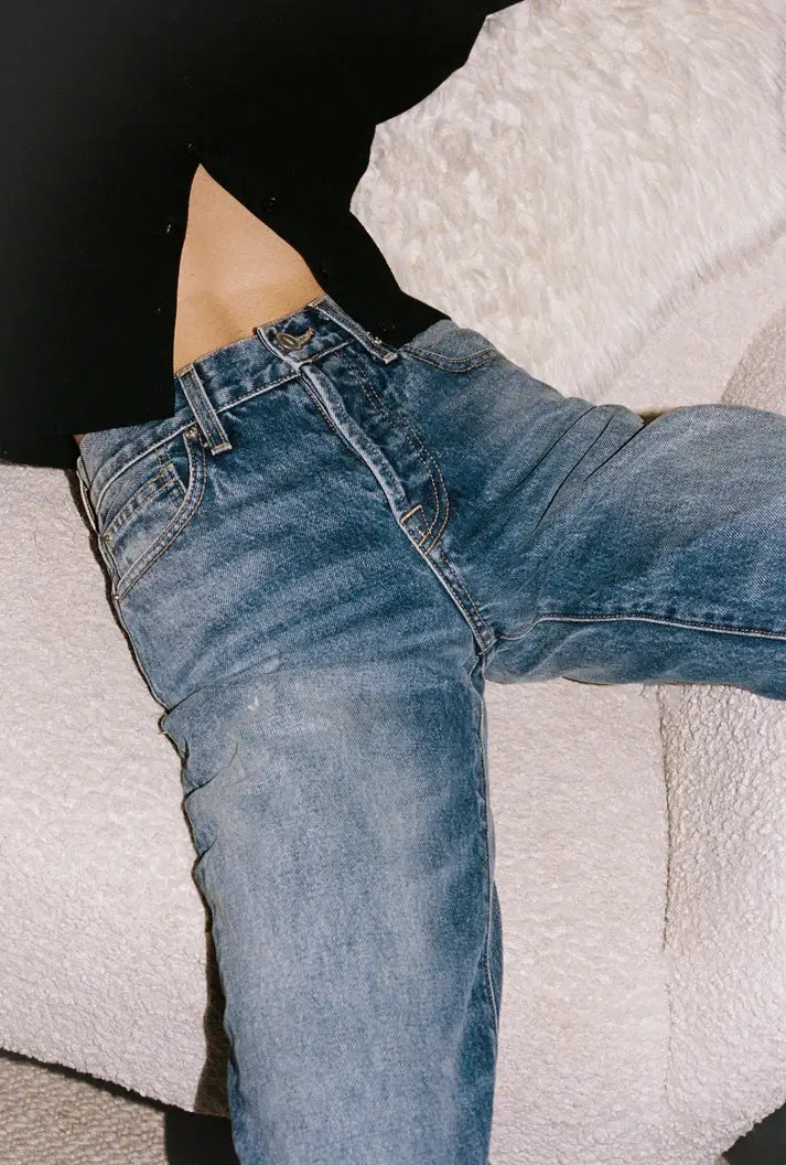Person wearing blue straight leg jeans on a textured white surface