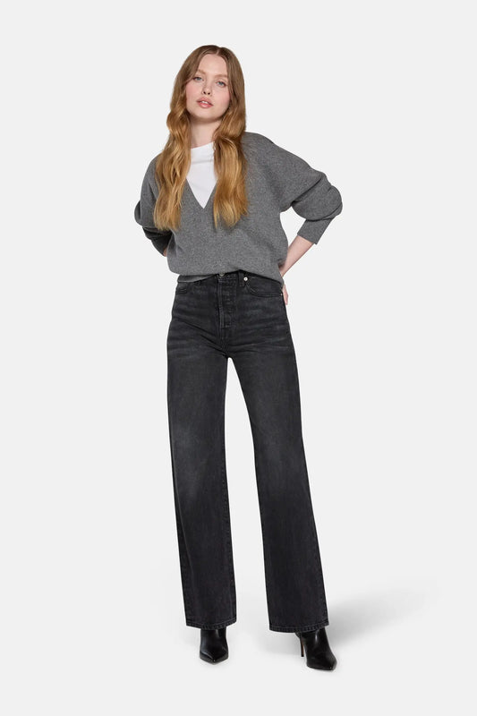a women standing in front of white background wearing grey top and charchoal color high rise straight leg jeans 