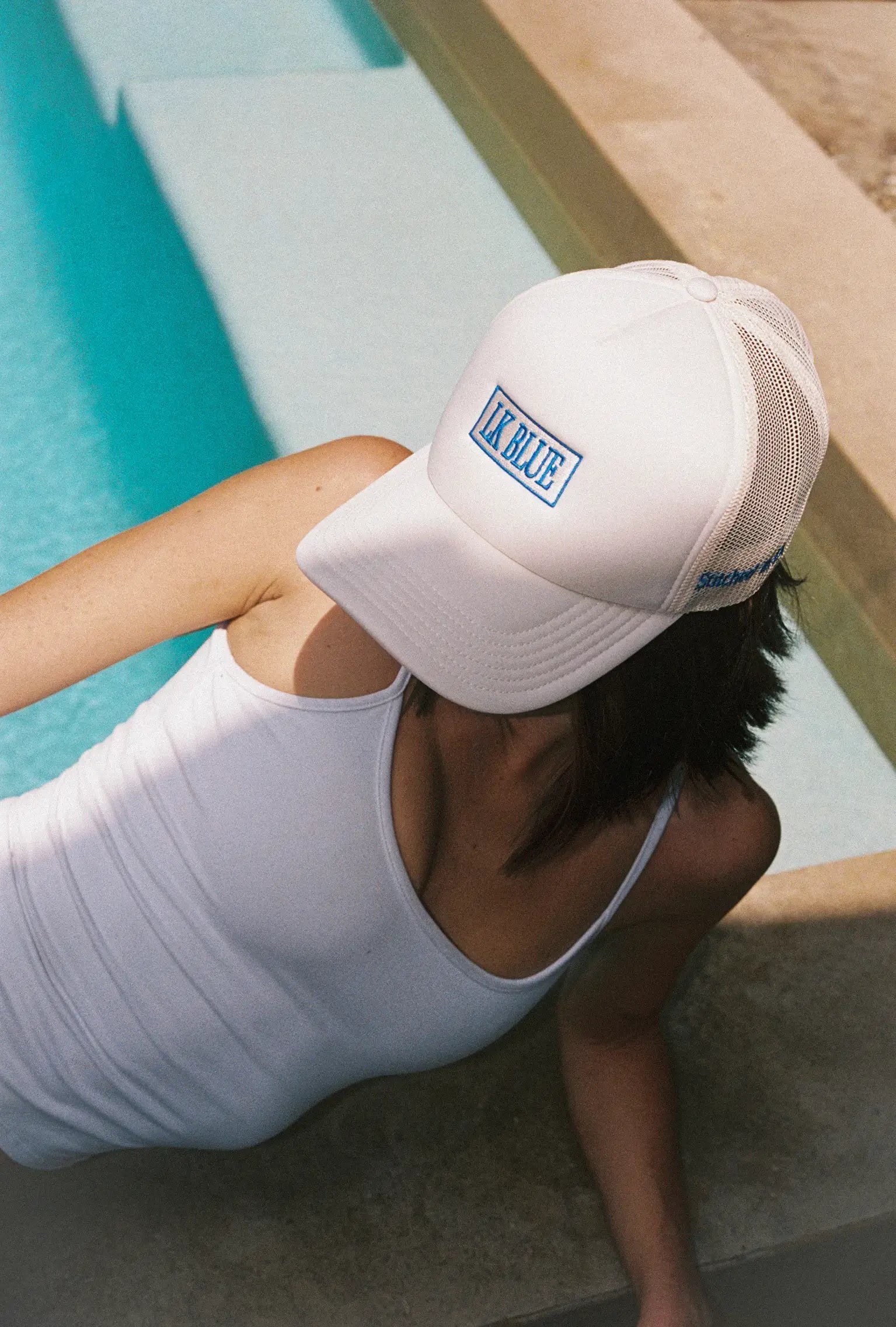 A person wearing a white cap with a logo of LKBLUE by a pool