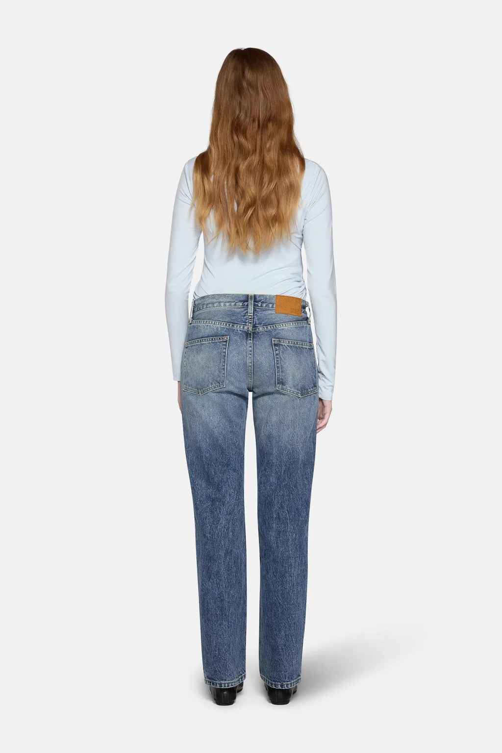 a women in front of white background wearing straight leg jeans in blue with back cover with hairs 