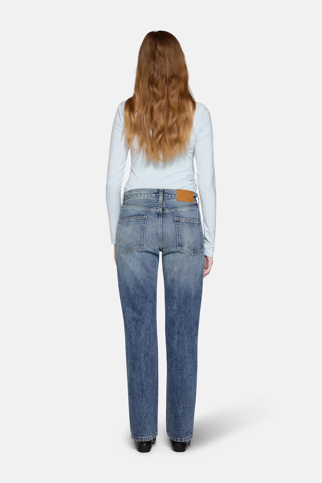 a women in front of white background wearing straight leg jeans in blue with back cover with hairs 