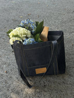 Black leather tote bag with flowers and a book on a concrete surface