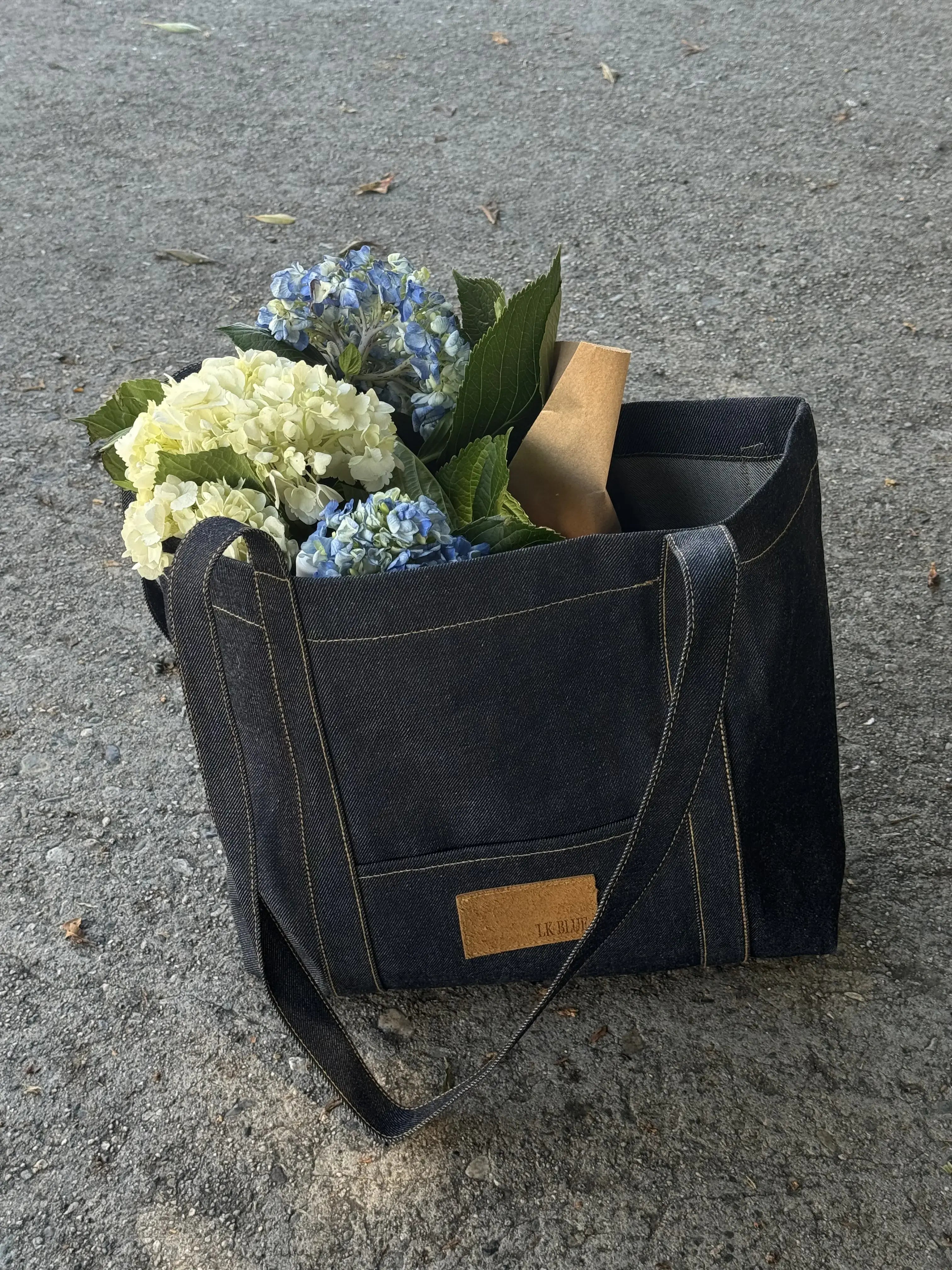 Black leather tote bag with flowers and a book on a concrete surface
