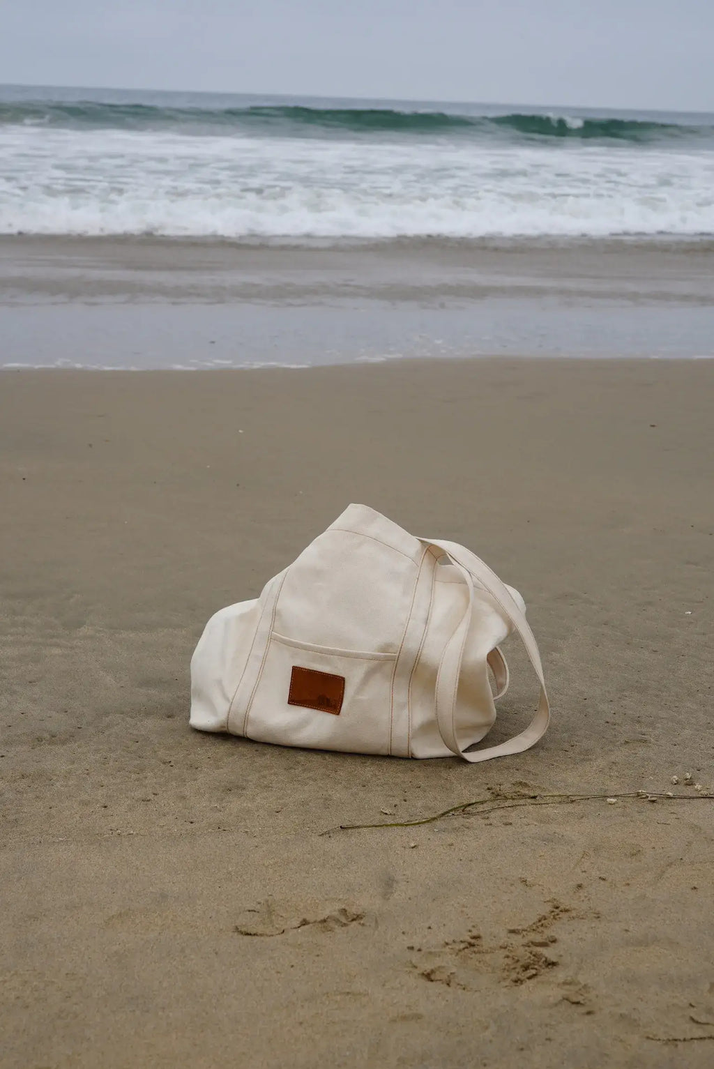 Beige bag on a sandy beach with ocean waves in the background
