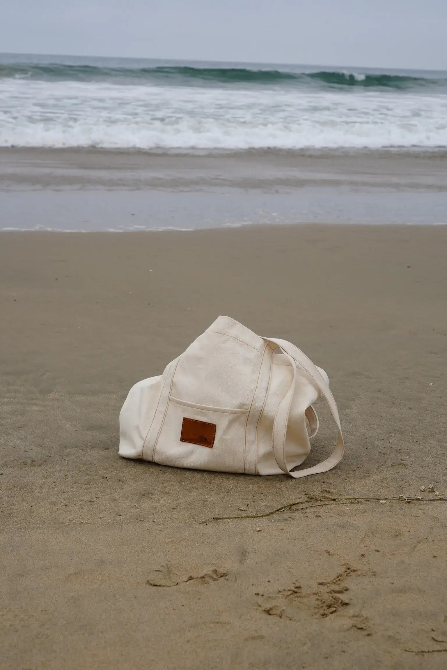 Beige bag on a sandy beach with ocean waves in the background