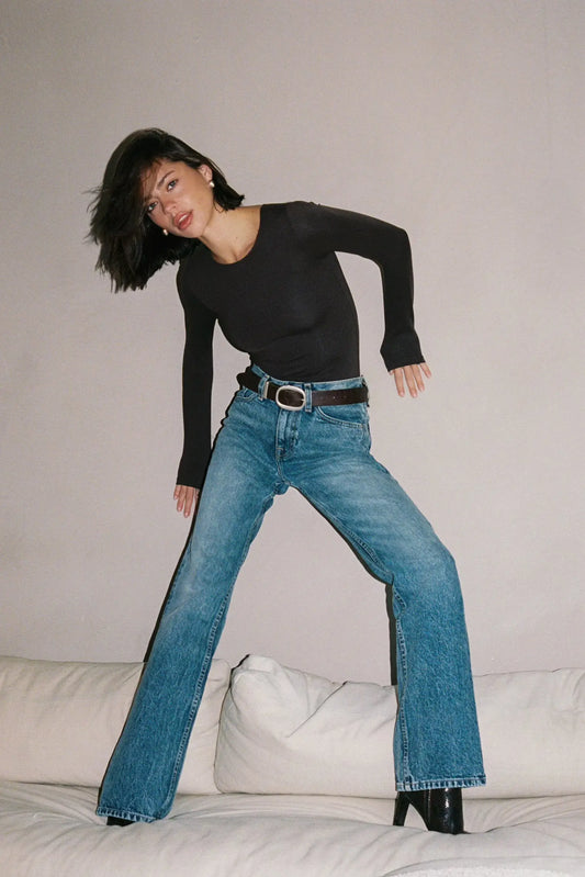 Woman wearing a black top and blue jeans standing on a white surface with a neutral background