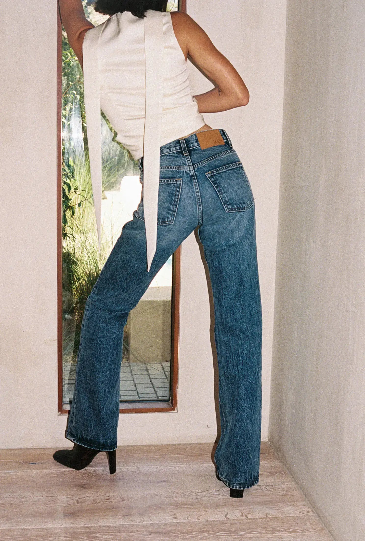 Person wearing blue jeans and a white top standing in front of a mirror.