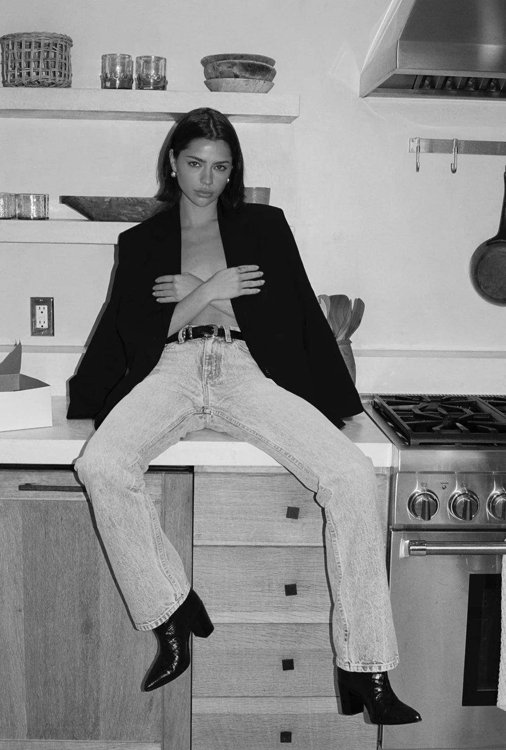 Person sitting on a kitchen counter wearing a black blazer and light-colored jeans.
