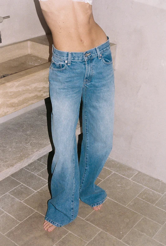 Person wearing blue sunfade shade denim jeans standing on a tiled floor.
