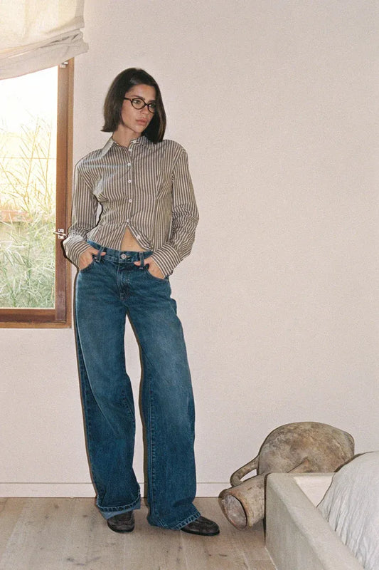 A woman wearing a checkered shirt and blue LA denim jeans is standing indoors.