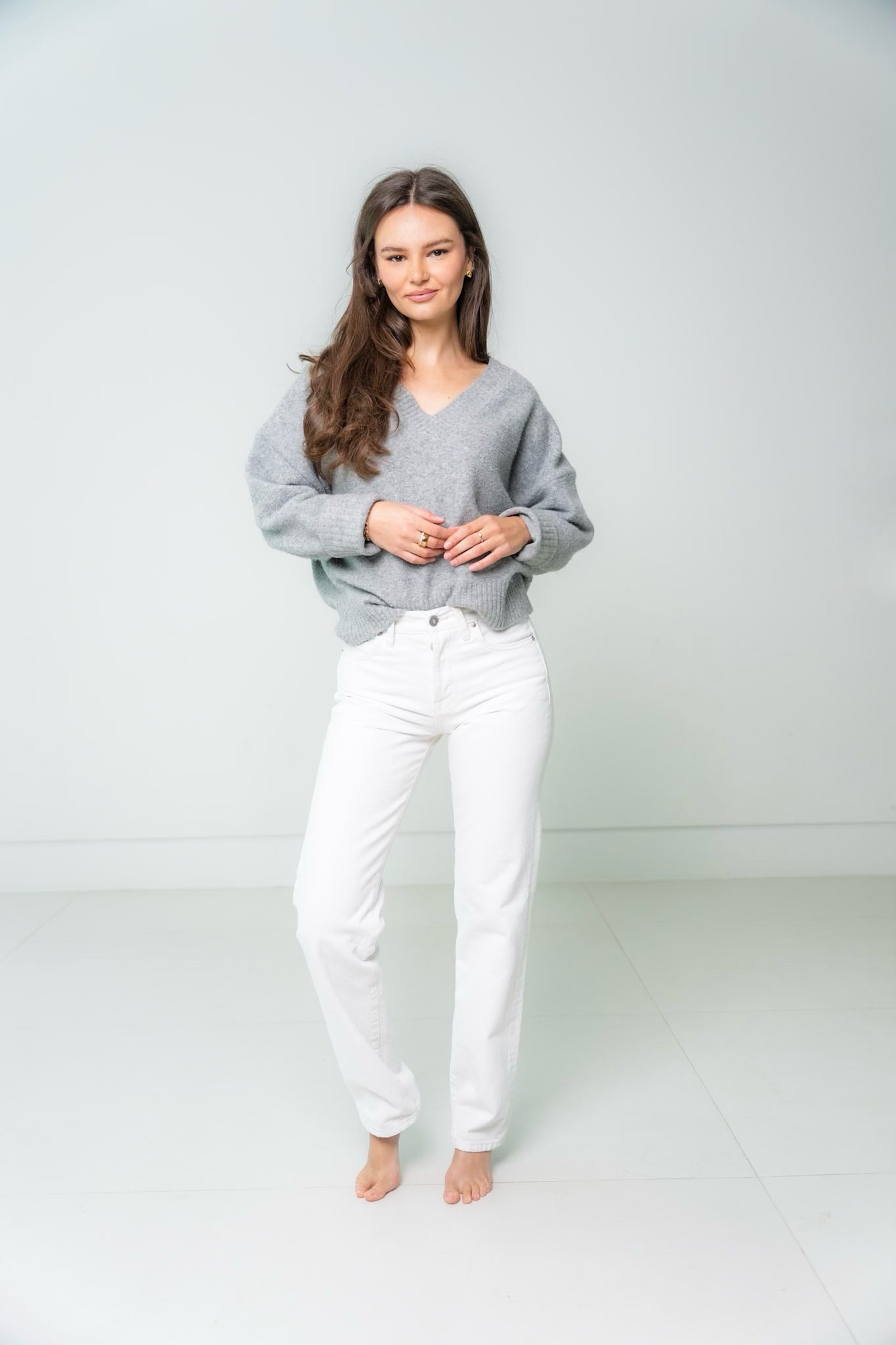 Woman wearing a gray sweater and white pants against a plain background