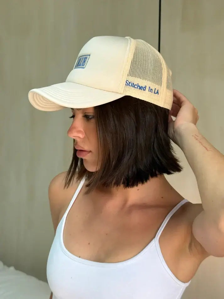 Woman wearing a beige trucker hat with text, indoors.