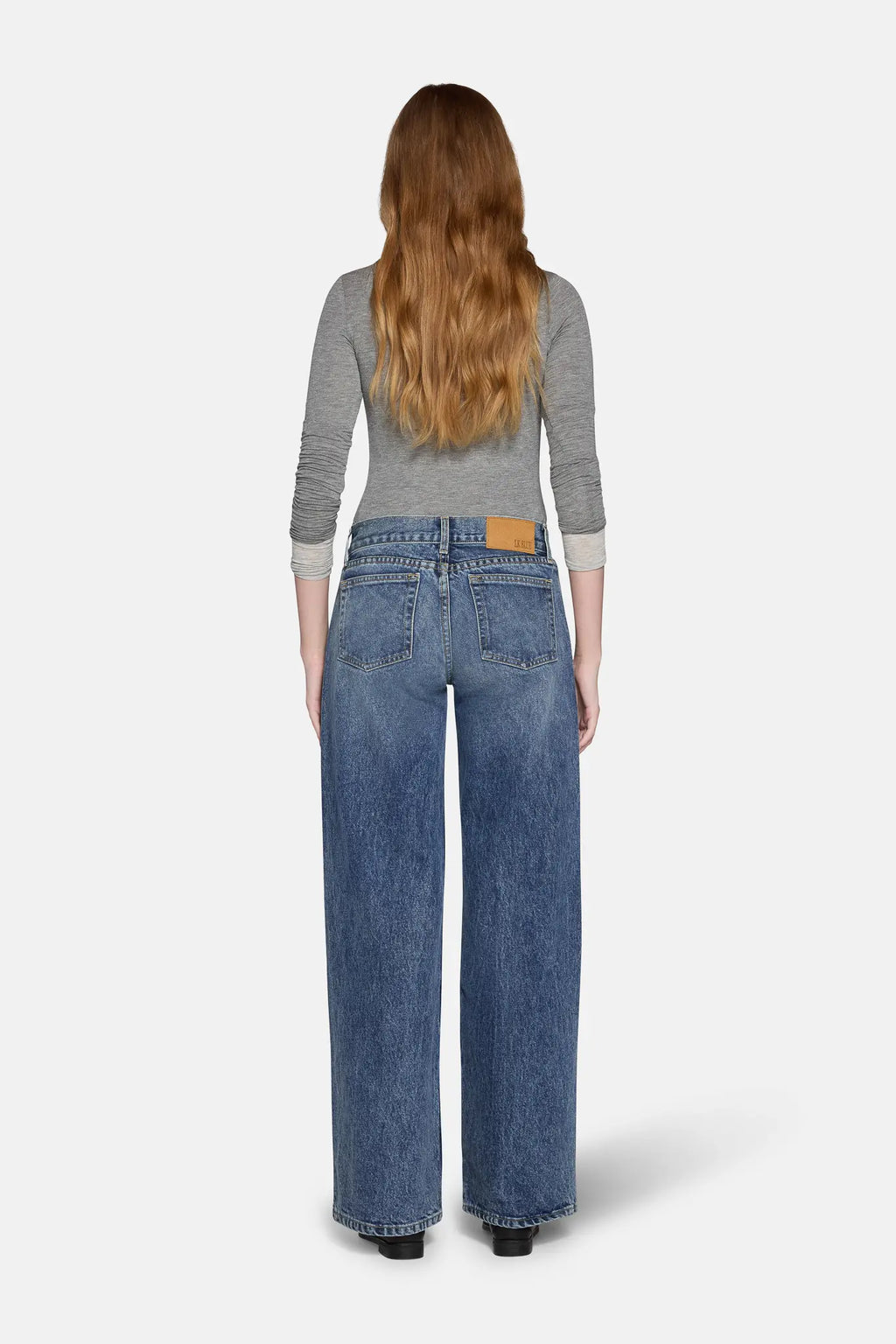 low rise baggy jeans in blue worn  by a women standing in front of white background 