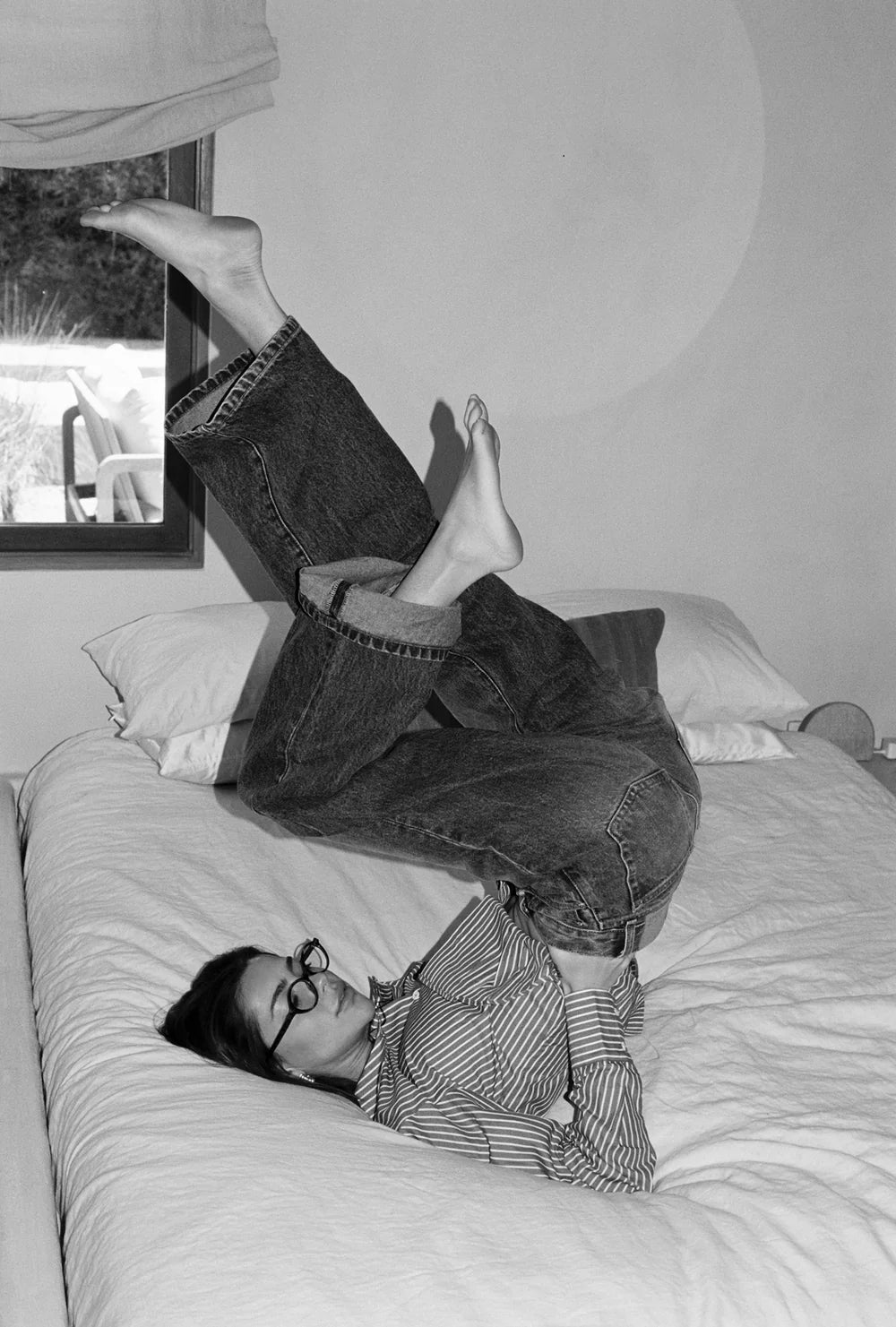 Person lying on a bed with legs stretched out, wearing denim jeans made in LA and a striped shirt.