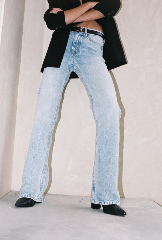 Person wearing light blue jeans and a black jacket with a plain background