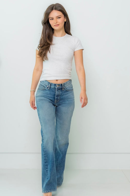 A woman wearing a white t-shirt and straight-leg blue denim jeans against a white background