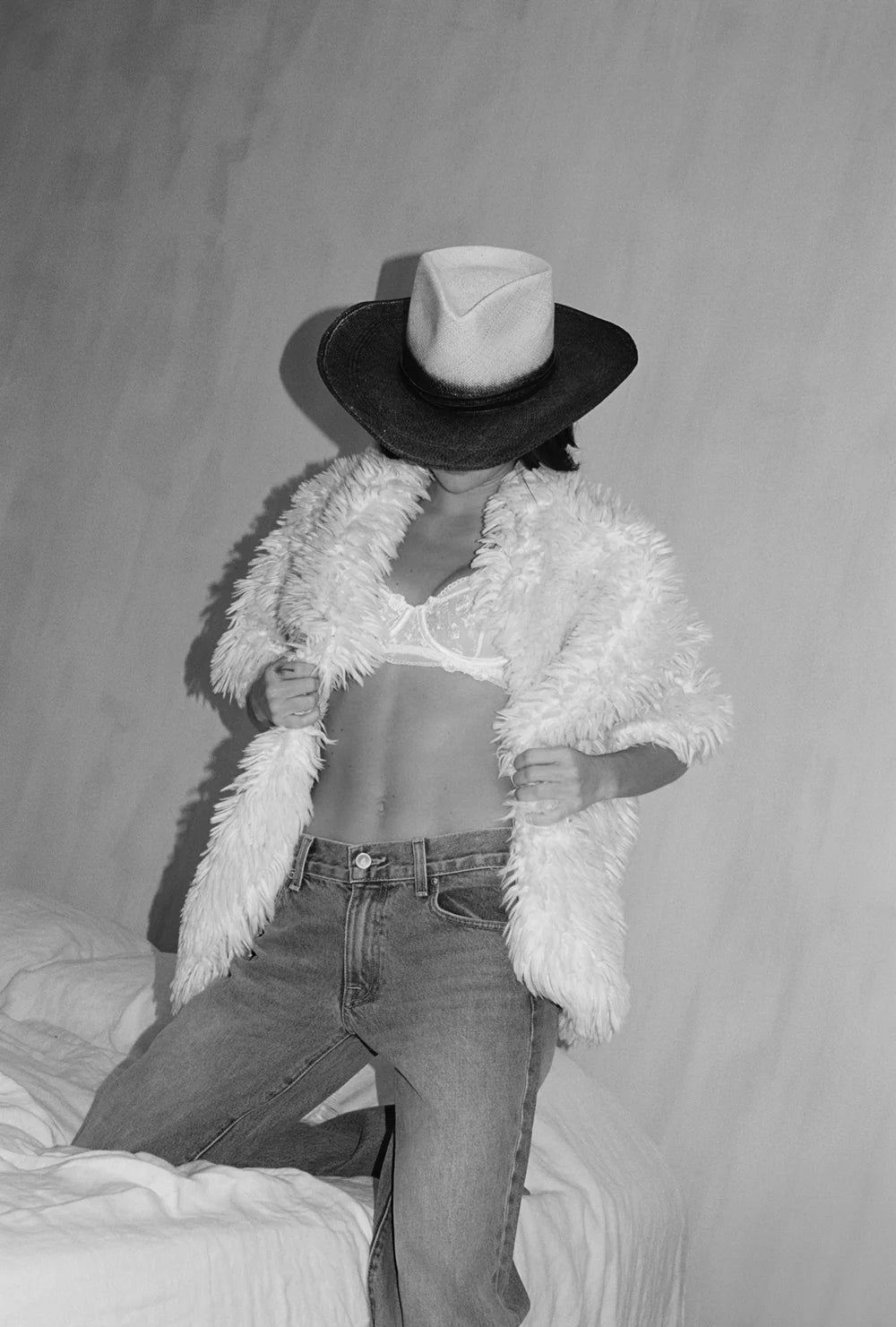 Person wearing a wide-brimmed hat, fluffy furr white jacket, and jeans against a plain background